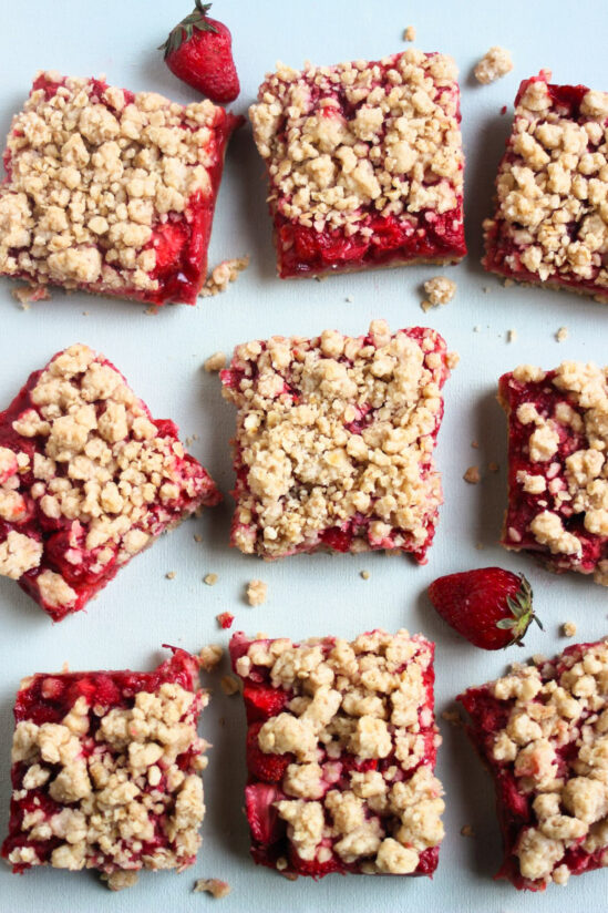 Strawberry bars and two fresh strawberries on a white surface, seen from above.