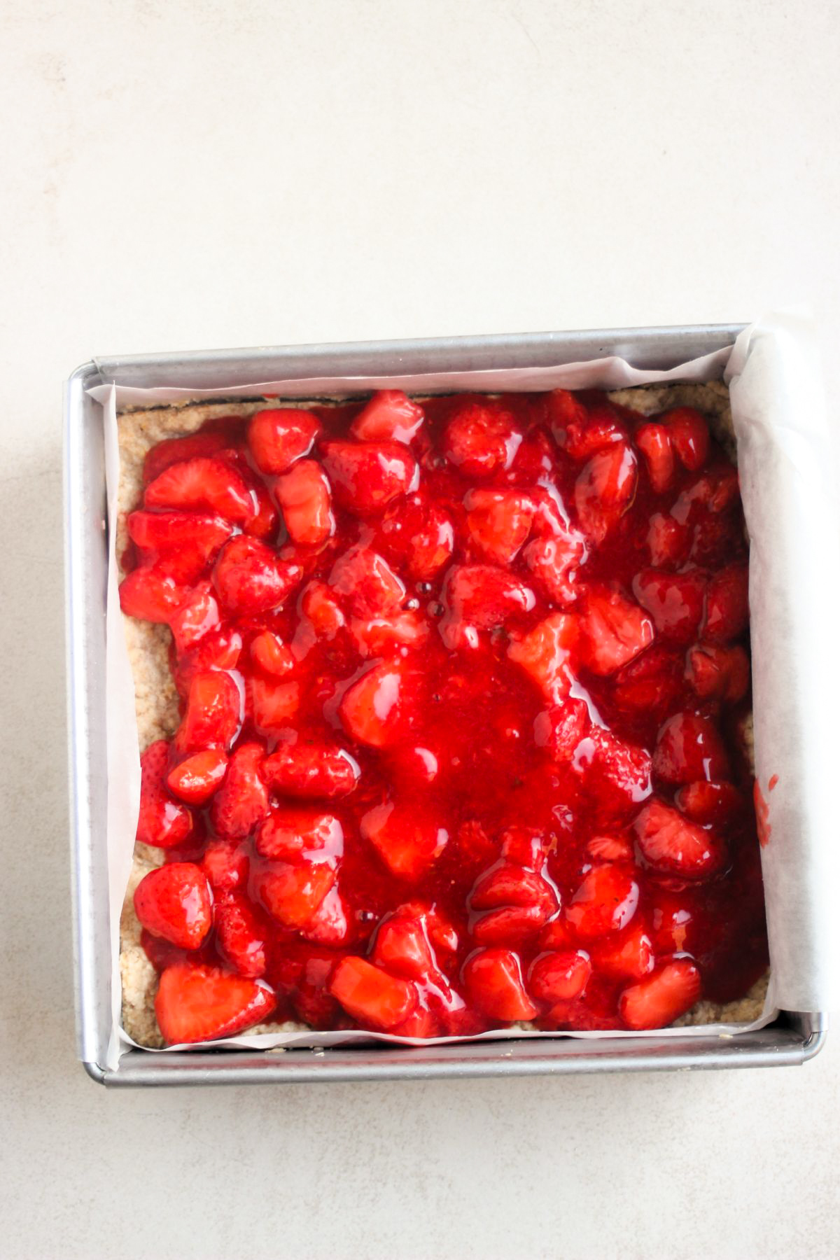 Strawberry sauce in a lined metal square pan. White background. Top view.