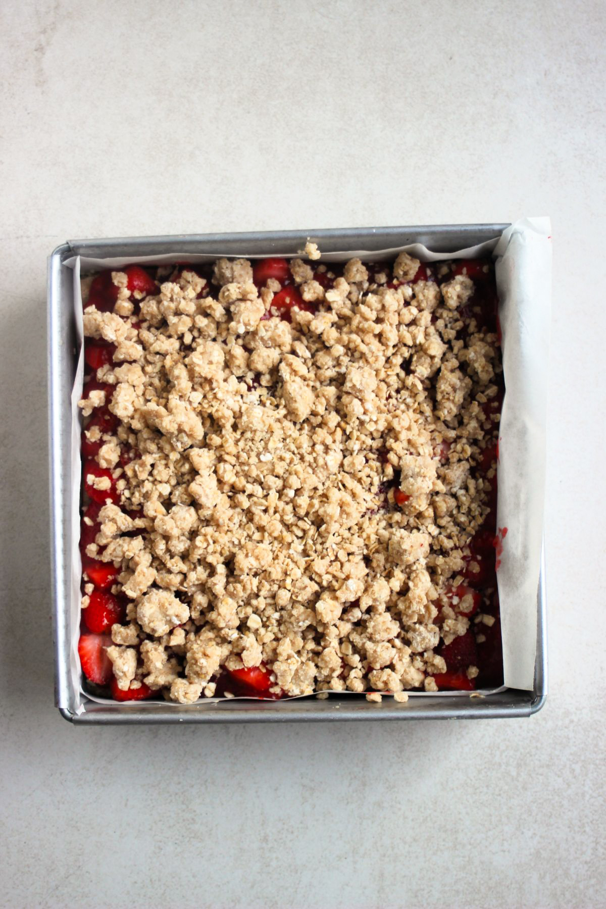 Strawberry bars before baking in a square metal pan. White background.