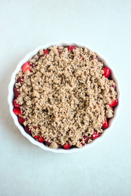 Top view of a round baking dish with fresh chopped strawberries and crumble topping before baking.