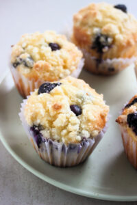 Blueberry streusel muffins in liners on an aqua-green plate.