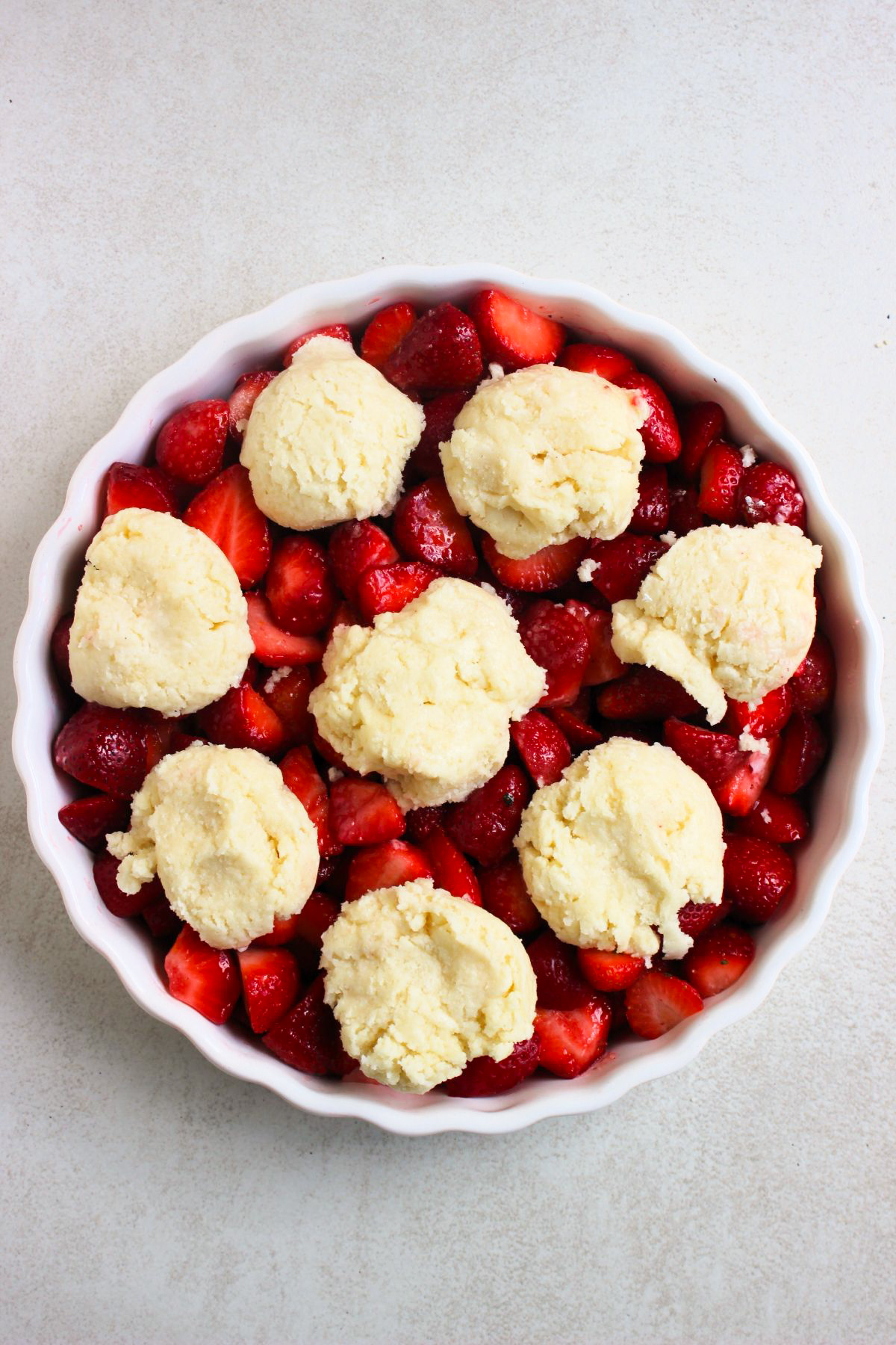 Top view of a round baking dish with chopped strawberries and balls of cookie dough.