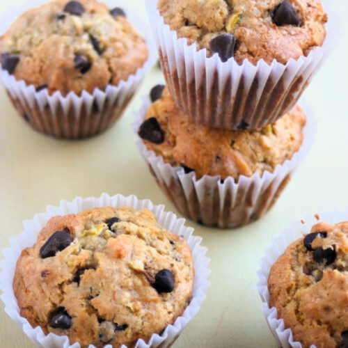 Zucchini chocolate chip muffins with liners on a light cream color surface.