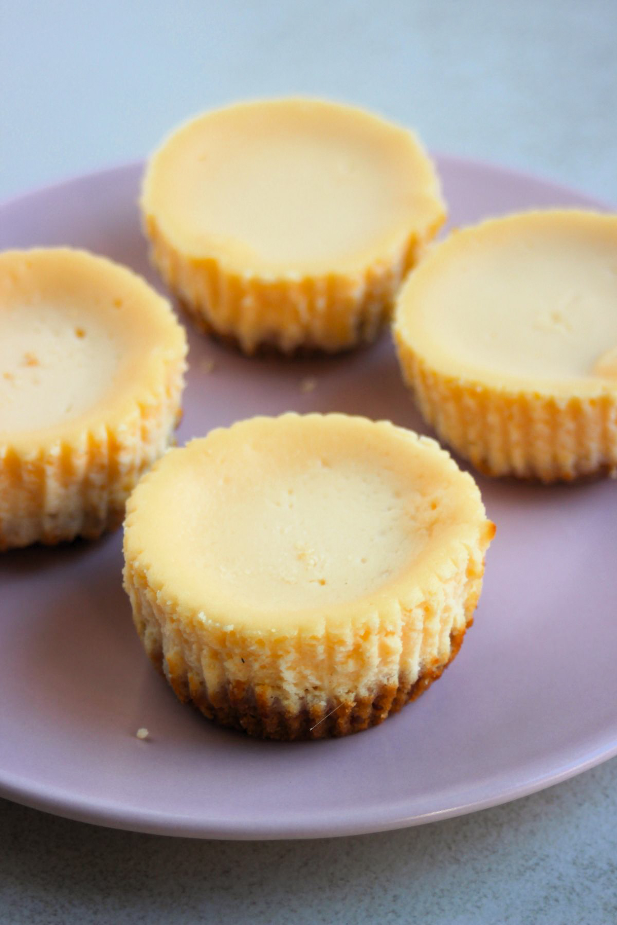 Four mini cheesecakes on a pink plate.