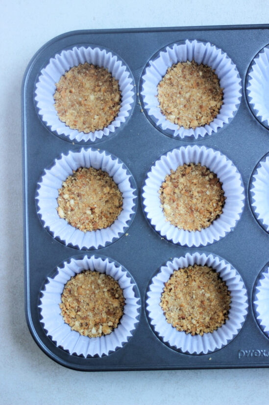 Top view of muffin pan with liners and cookie crust at the bottom of each liner.