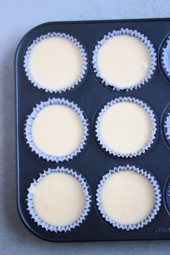 Top view of muffin pan with liners with a white mixture.