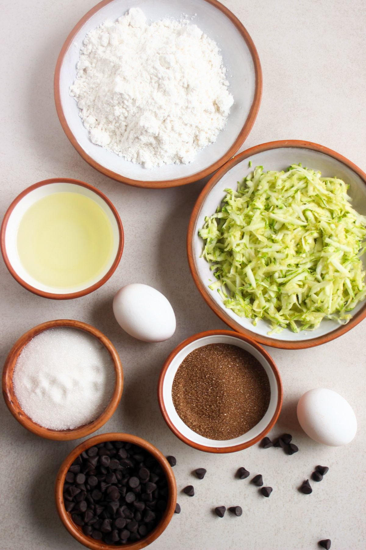 Top view of zucchini chocolate chip muffins ingredients on a white surface.