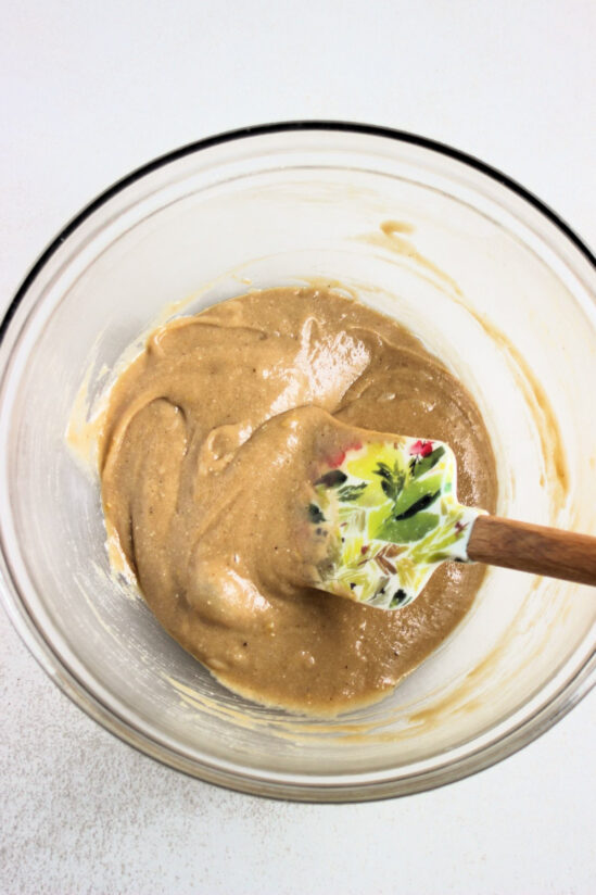 Glass bowl with a light brown mixture and a rubber spatula.