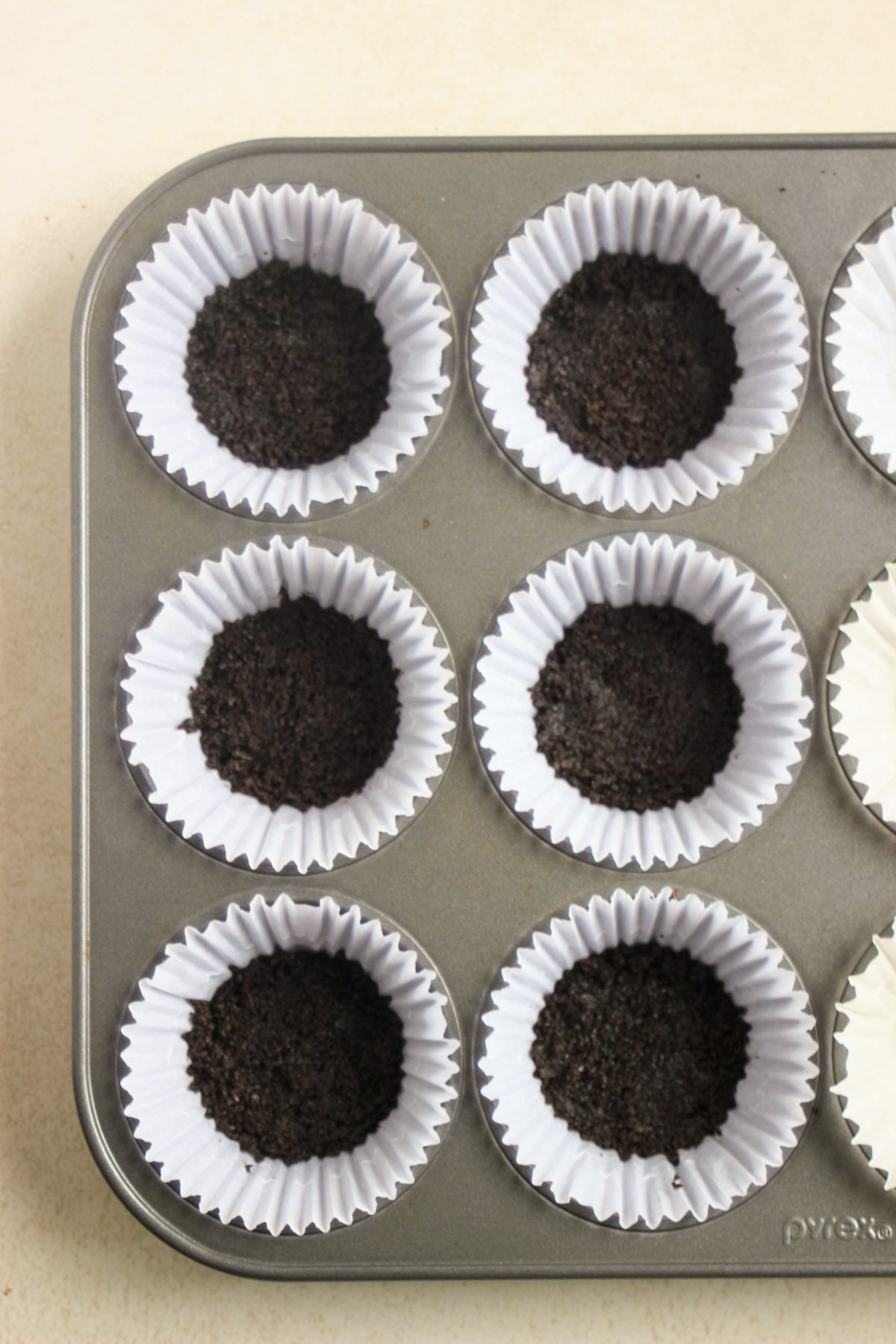 Top view of a muffin pan with liners and filled with chocolate cookie crust.