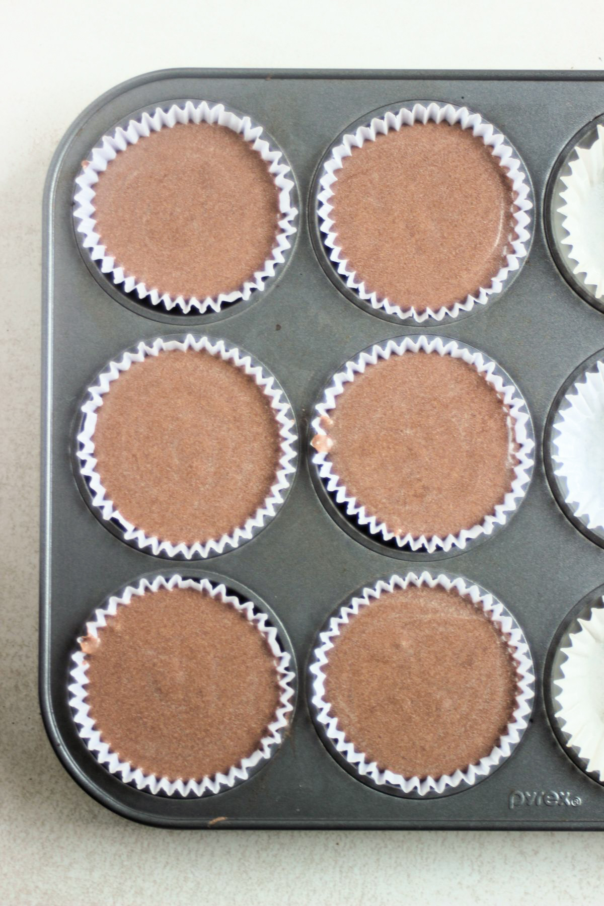 Top view of a muffin pan with liners and filled with raw chocolate cheesecake mixture.
