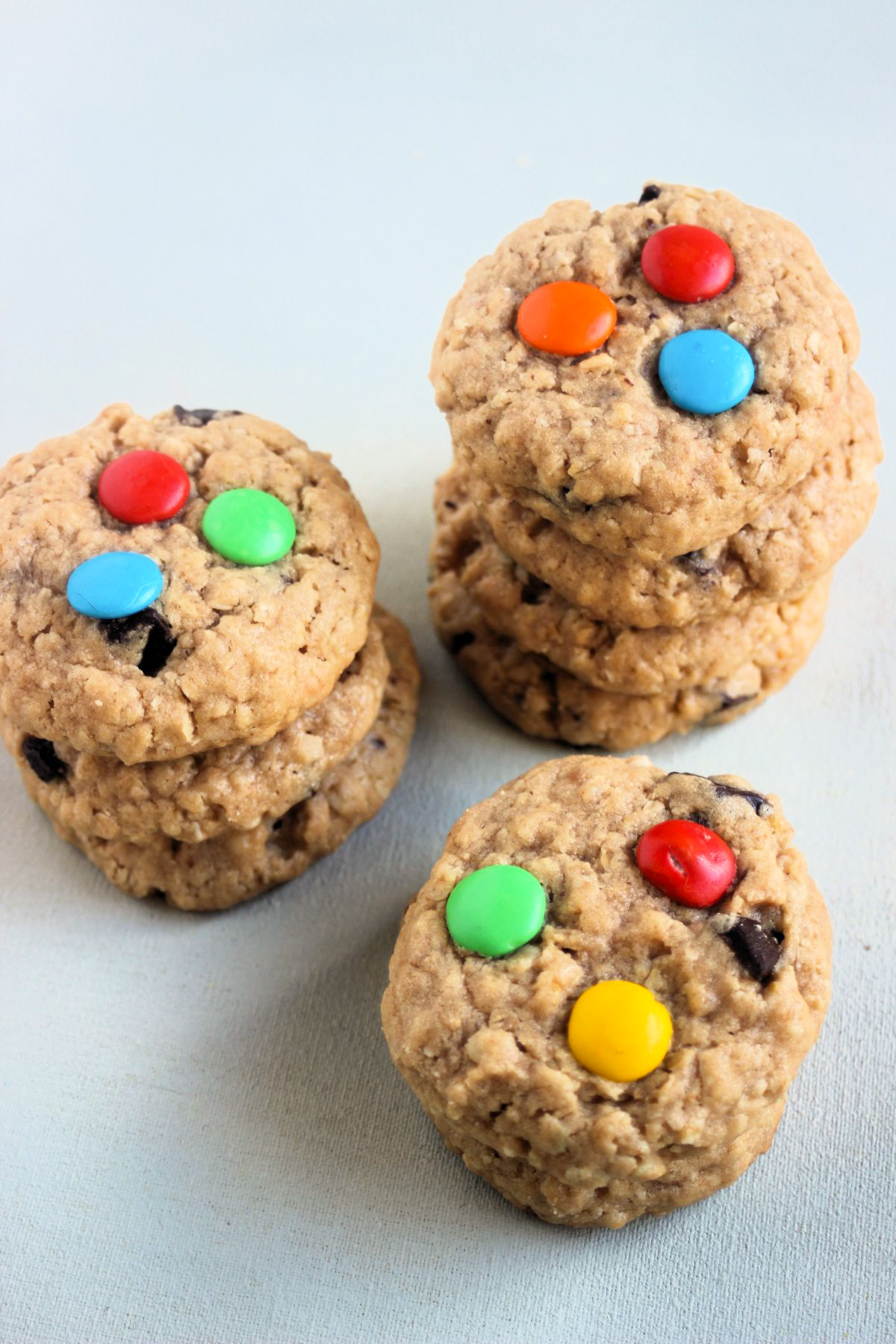 Three monster cookies stacked on a white surface.