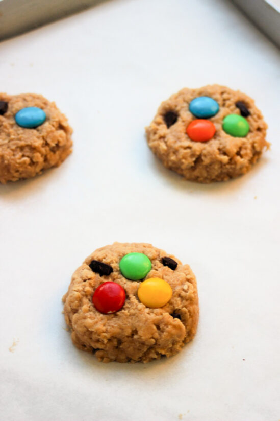 Monster cookie dough on parchment paper with the candies on top before baking.