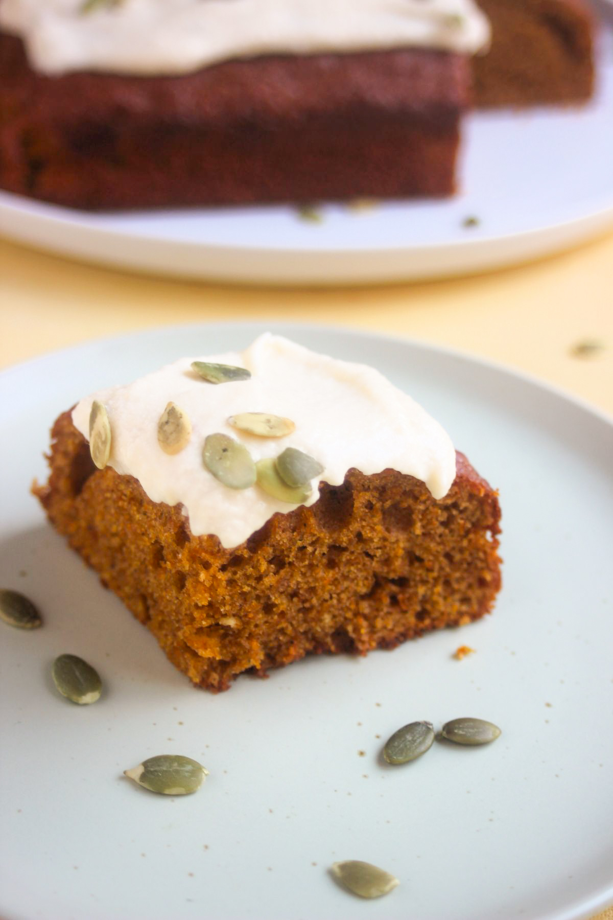 Pumpkin cake with frosting and pumpkin seeds on an aqua-green plate.