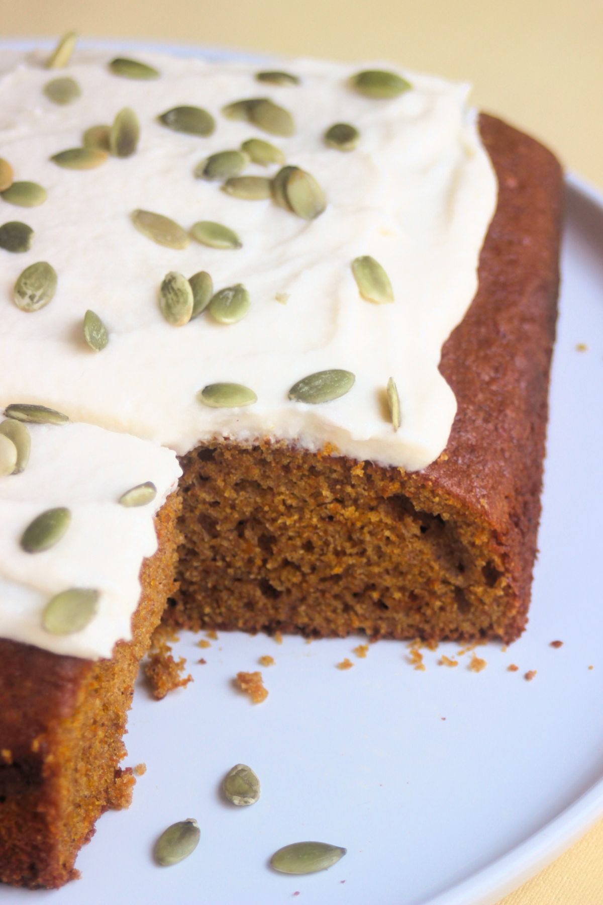 Pumpkin cake with frosting and pumpkin seeds on a white plate.