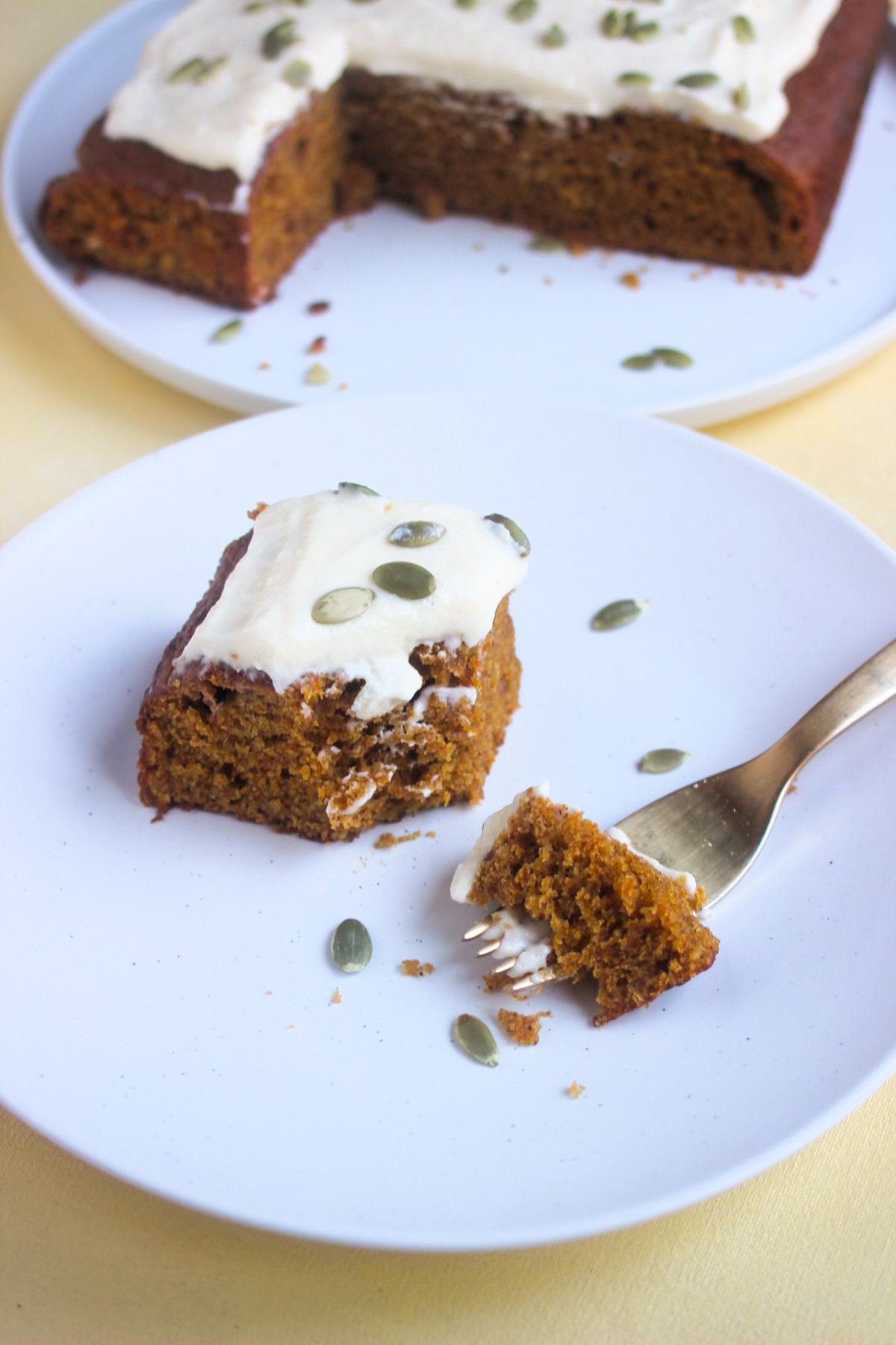 Pumpkin pie with frosting and pumpkin seeds, without a slice, on a white plate. A golden fork with a piece of pie.