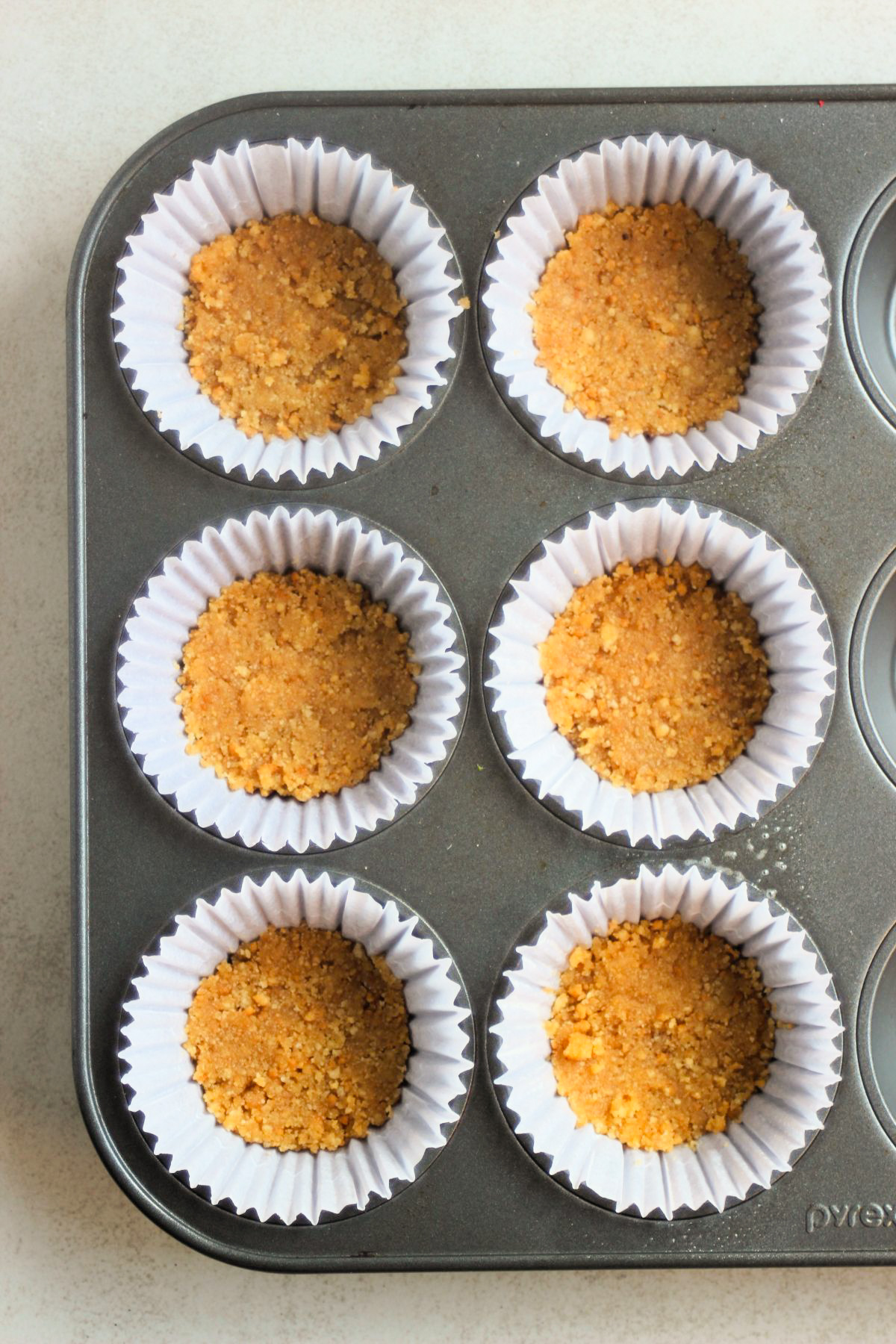 Top view of muffin pan with liners filled with cookie crust.
