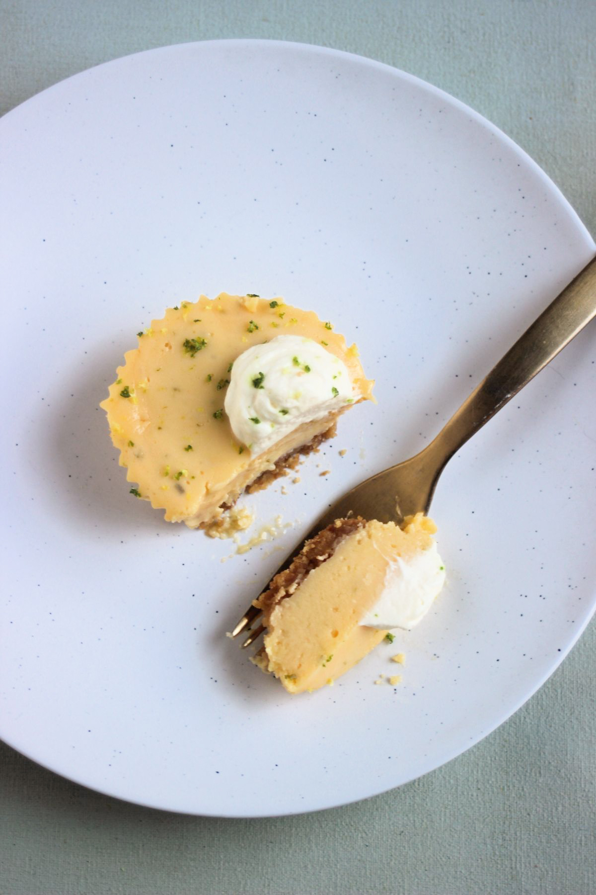 Top view of a mini key lime pie with whipped cream without a piece on a white plate. A golden fork with a piece of the cake.