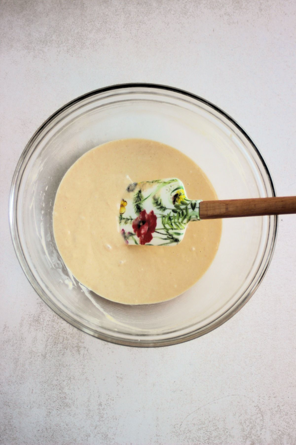 Glass bowl with a light yellow mixture and a rubber spatula.