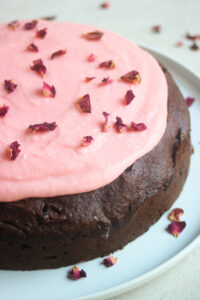 Chocolate beet cake with pink frosting and rose leaves on a white plate.