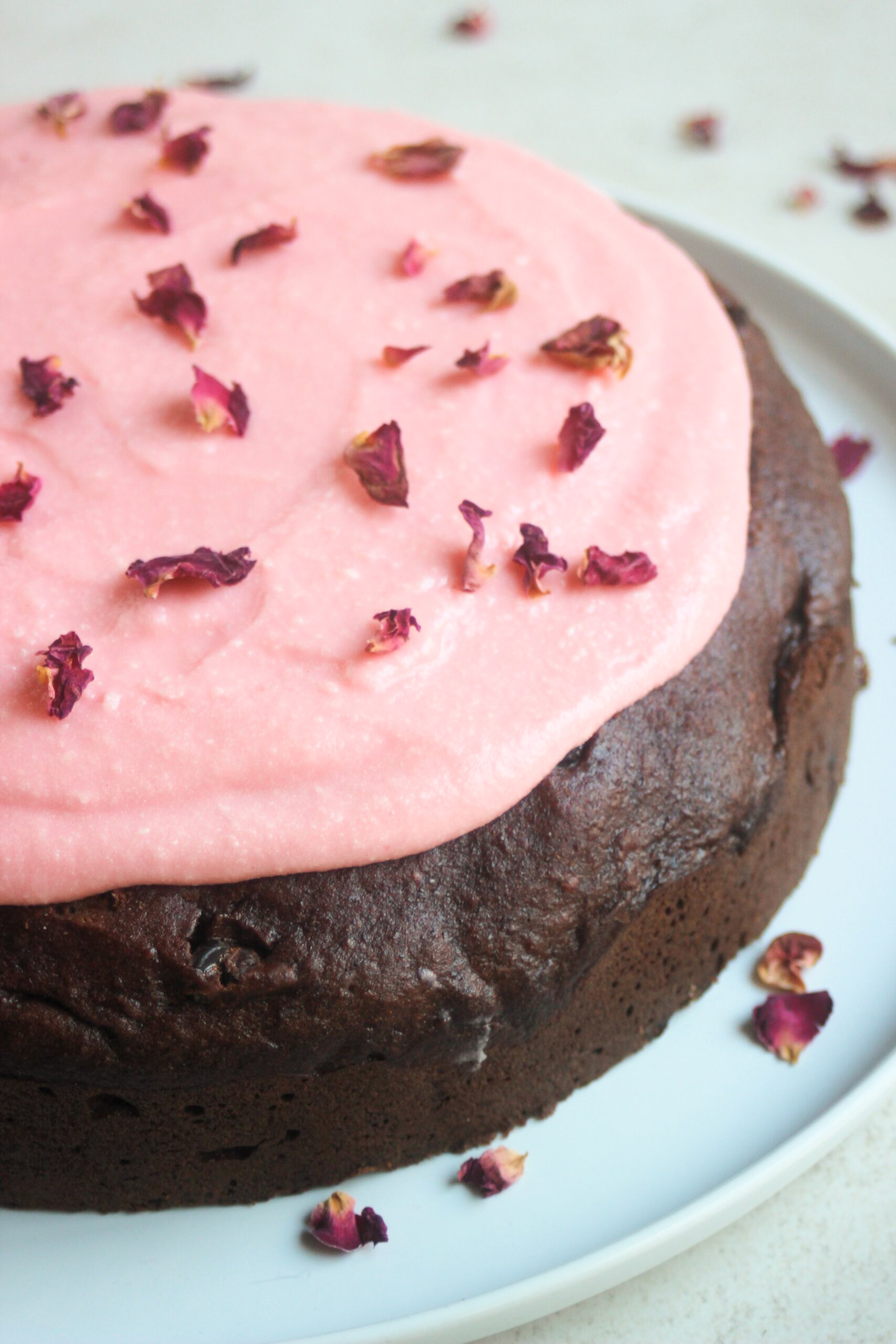 Chocolate beet cake with pink frosting and rose leaves on a white plate.