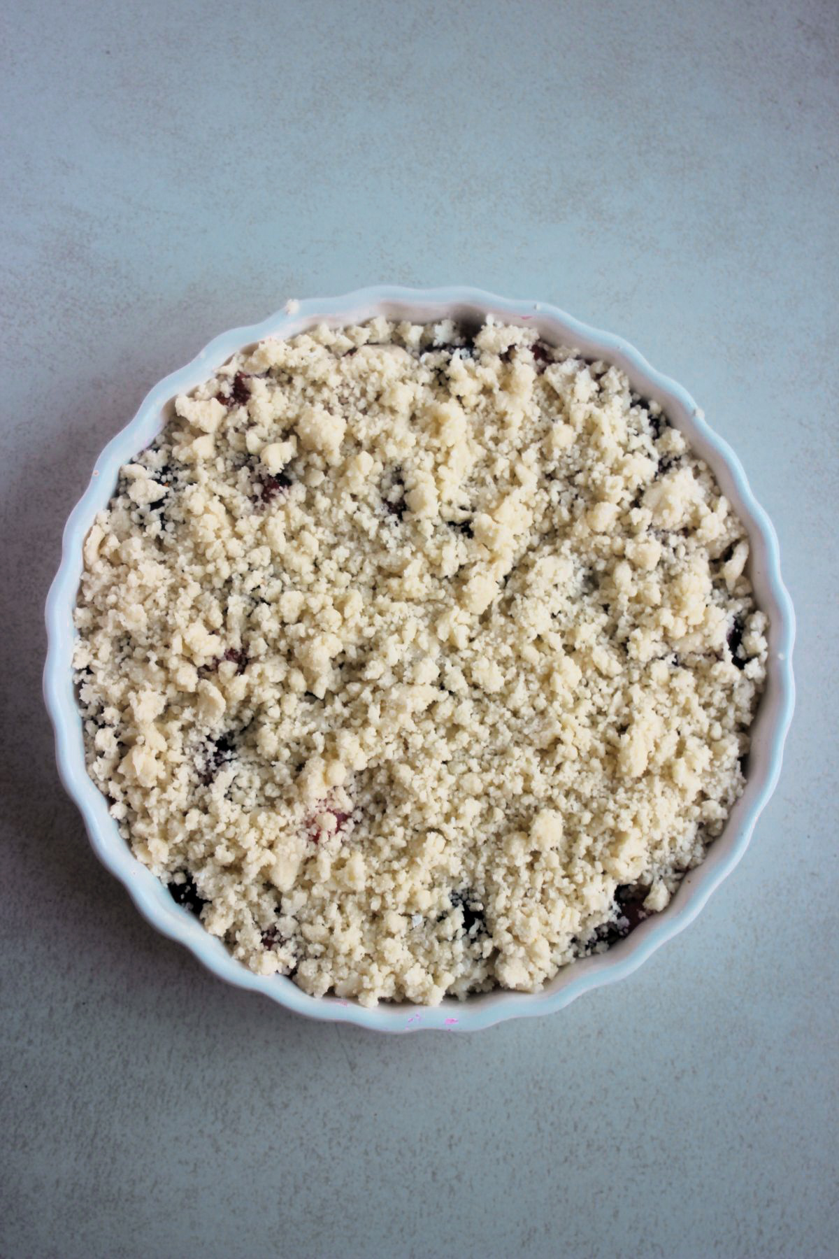 Top view of a round baking dish with plum crumble before baking.