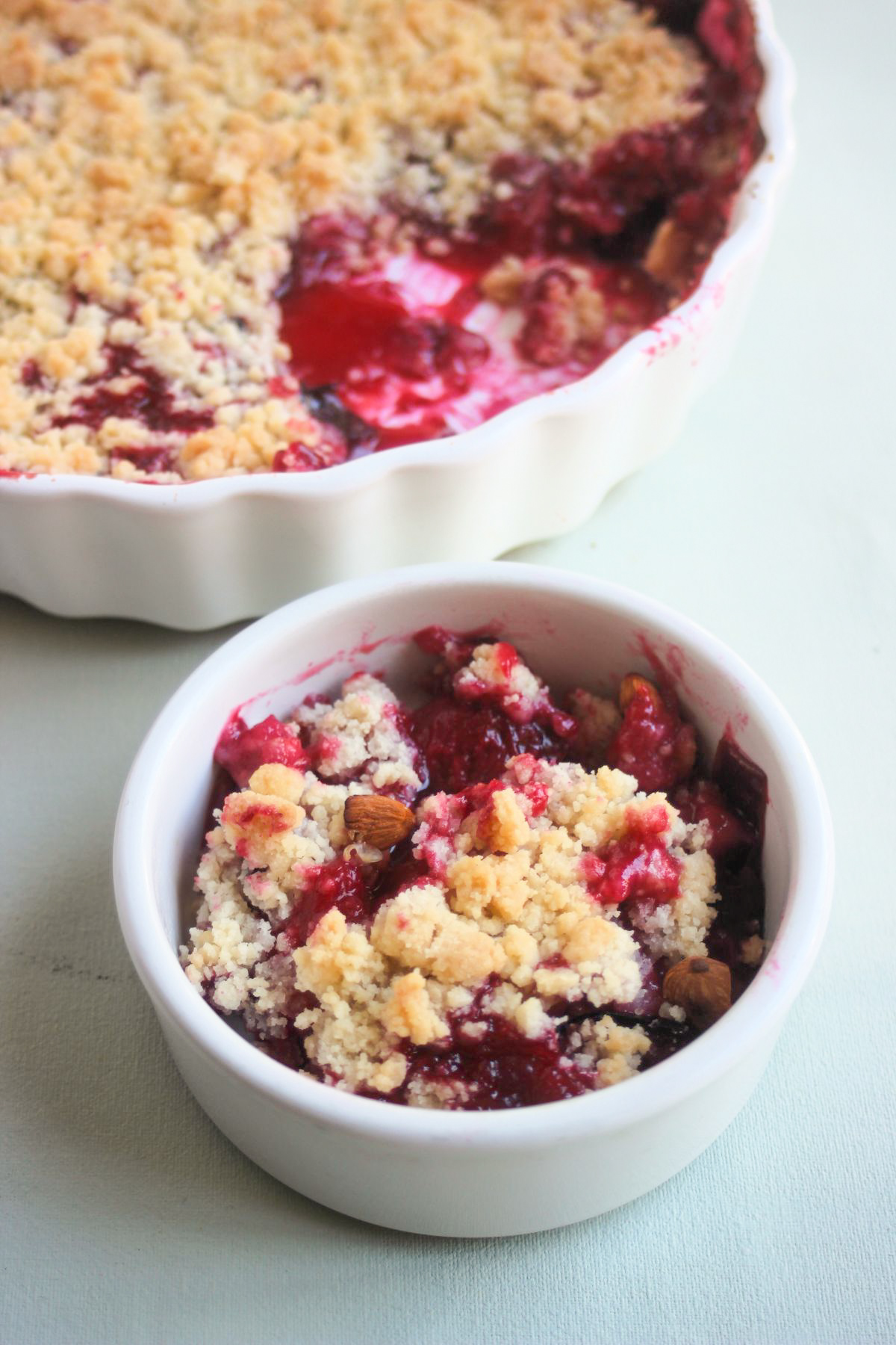 Small bowl with plum crumble. Whole crumble behind on a baking dish.
