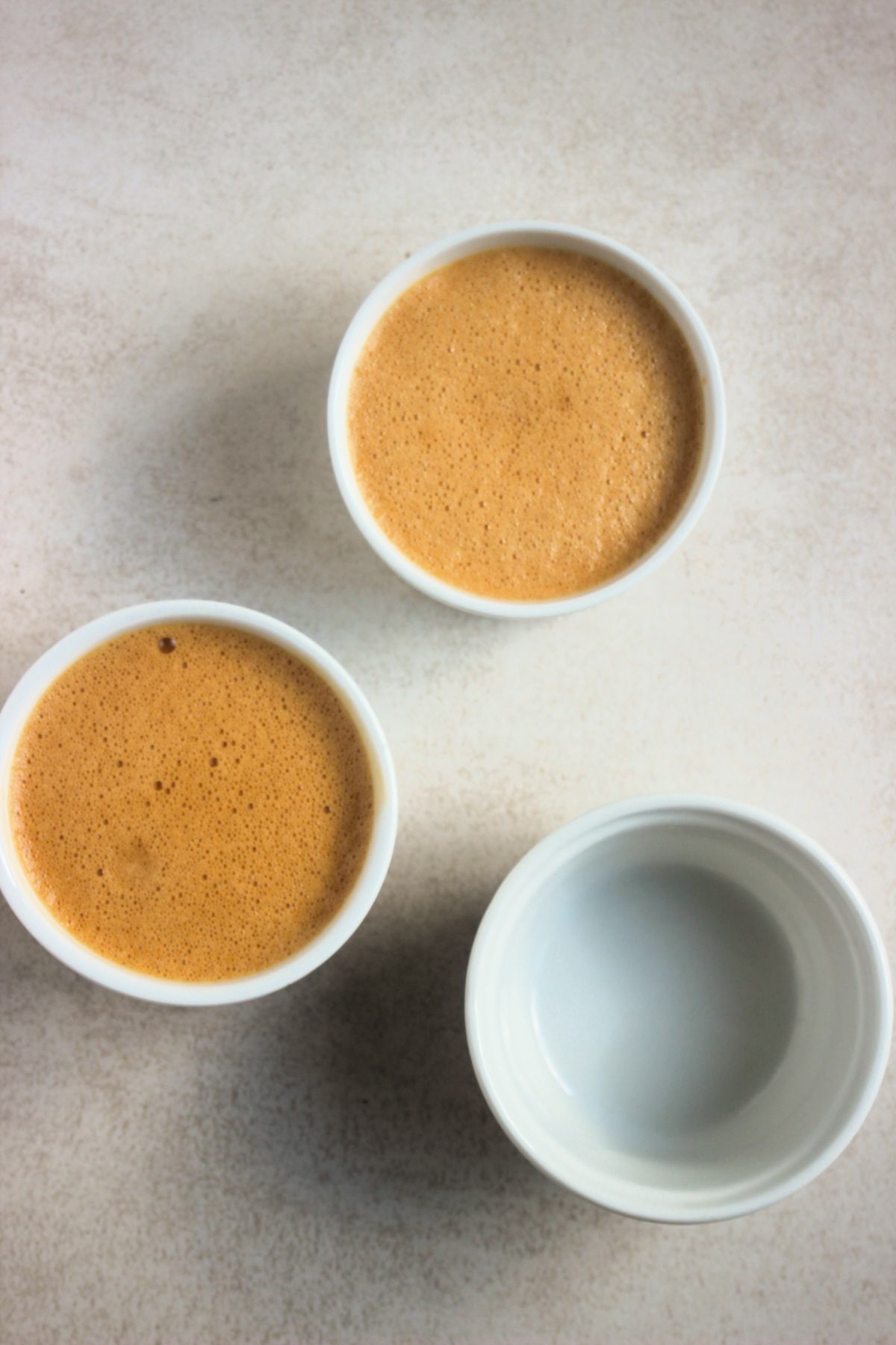 Top view of three ramekins, two filled with caramel-coloured mixture.