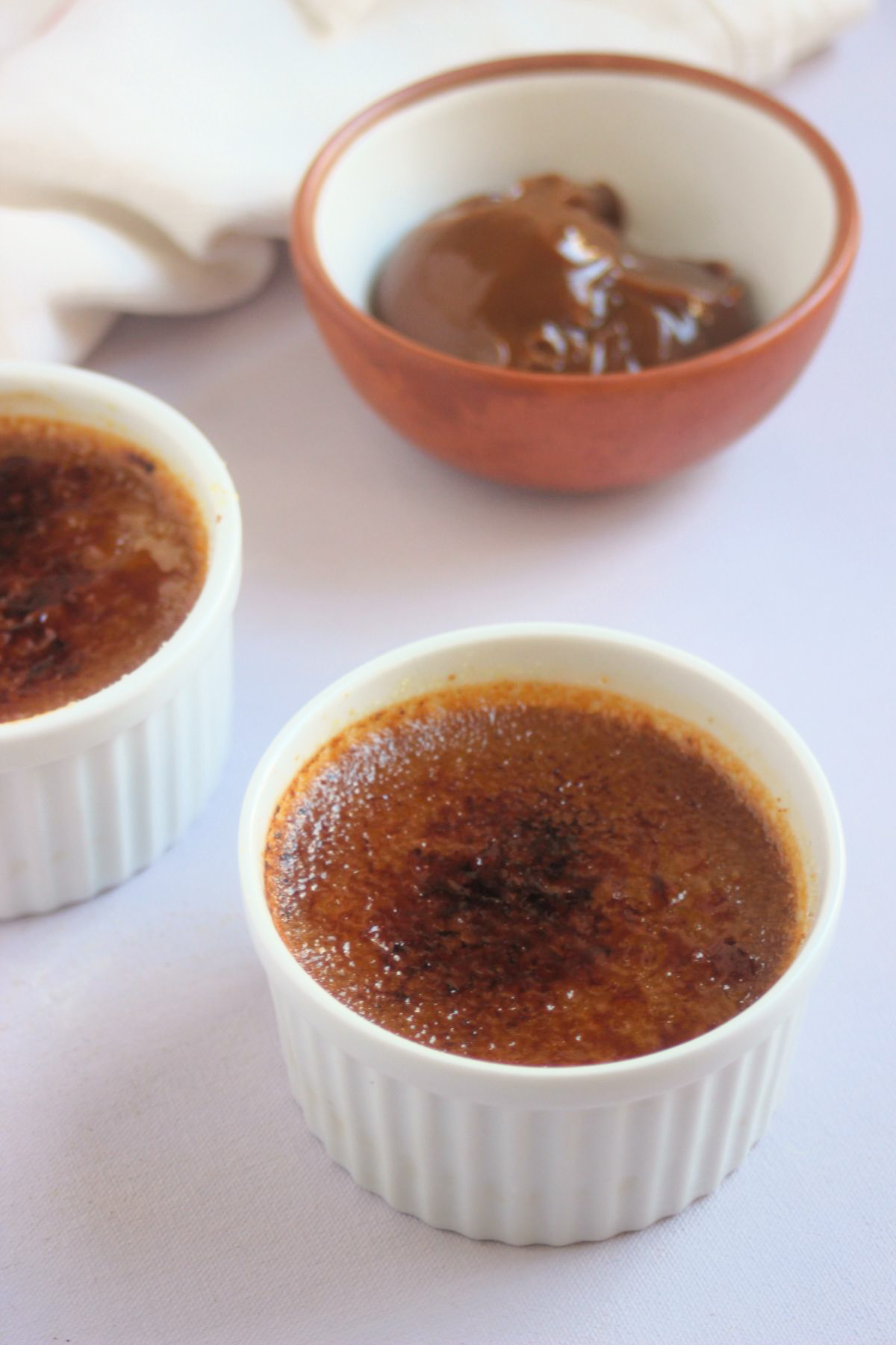 Ramekin with caramel creme brulee with the surface caramelized. Behind a tiny bowl with dulce de leche.