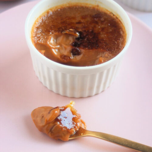 A partially eaten crème brûlée on a pink plate and a spoon with crème brûlée.