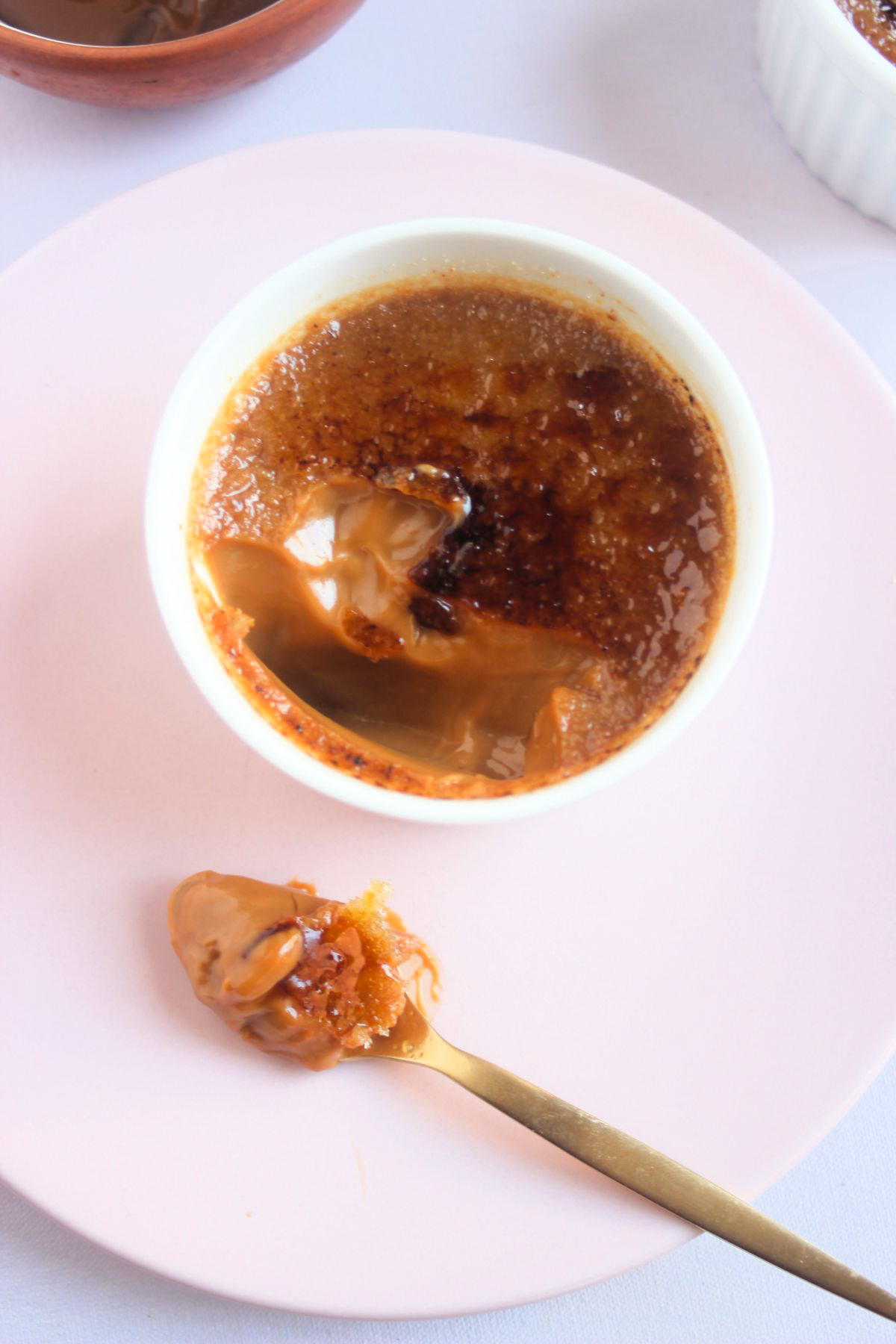 Top view of a partially eaten crème brûlée on a pink plate and a spoon with crème brûlée.
