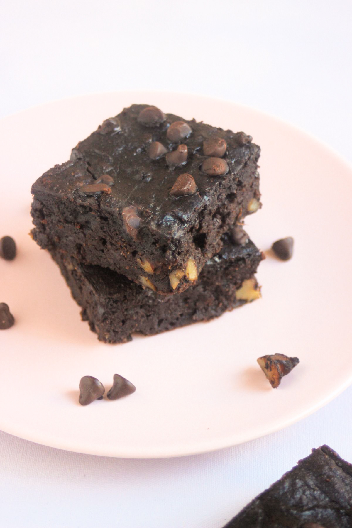 Stack of two sweet potato brownies on a pink plate. Chocolate chips are scattered on the plate.