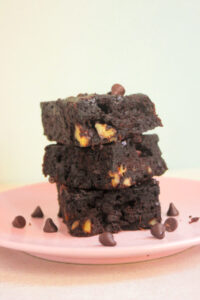 Front view of a stack of three sweet potato brownies on a pink plate. Chocolate chips are scattered on the plate.
