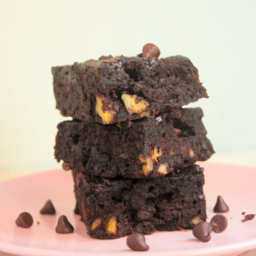 Front view of a stack of three sweet potato brownies on a pink plate. Chocolate chips are scattered on the plate.