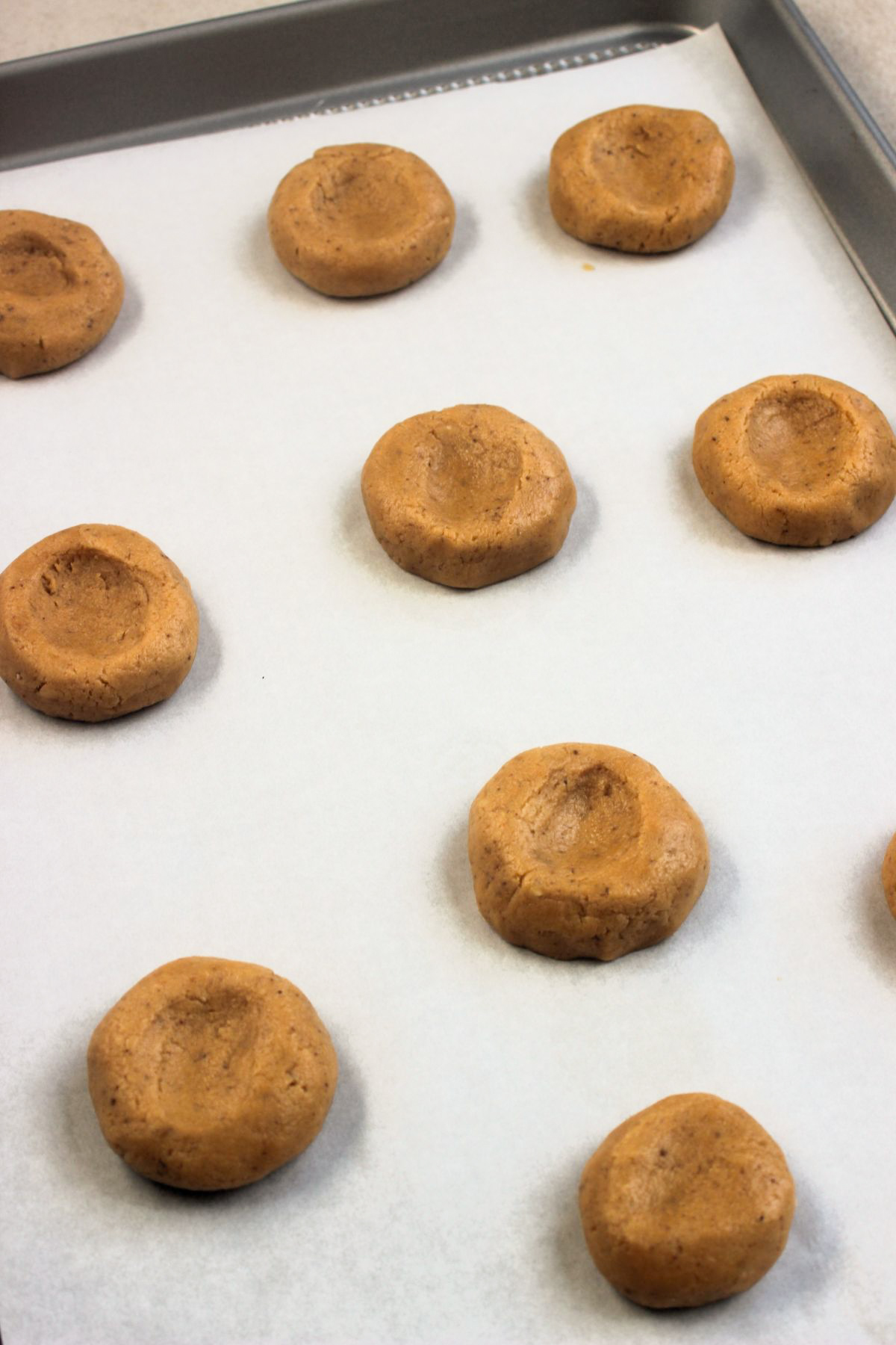 Peanut butter thumbprint cookies dough before baking on parchment paper on a baking sheet.