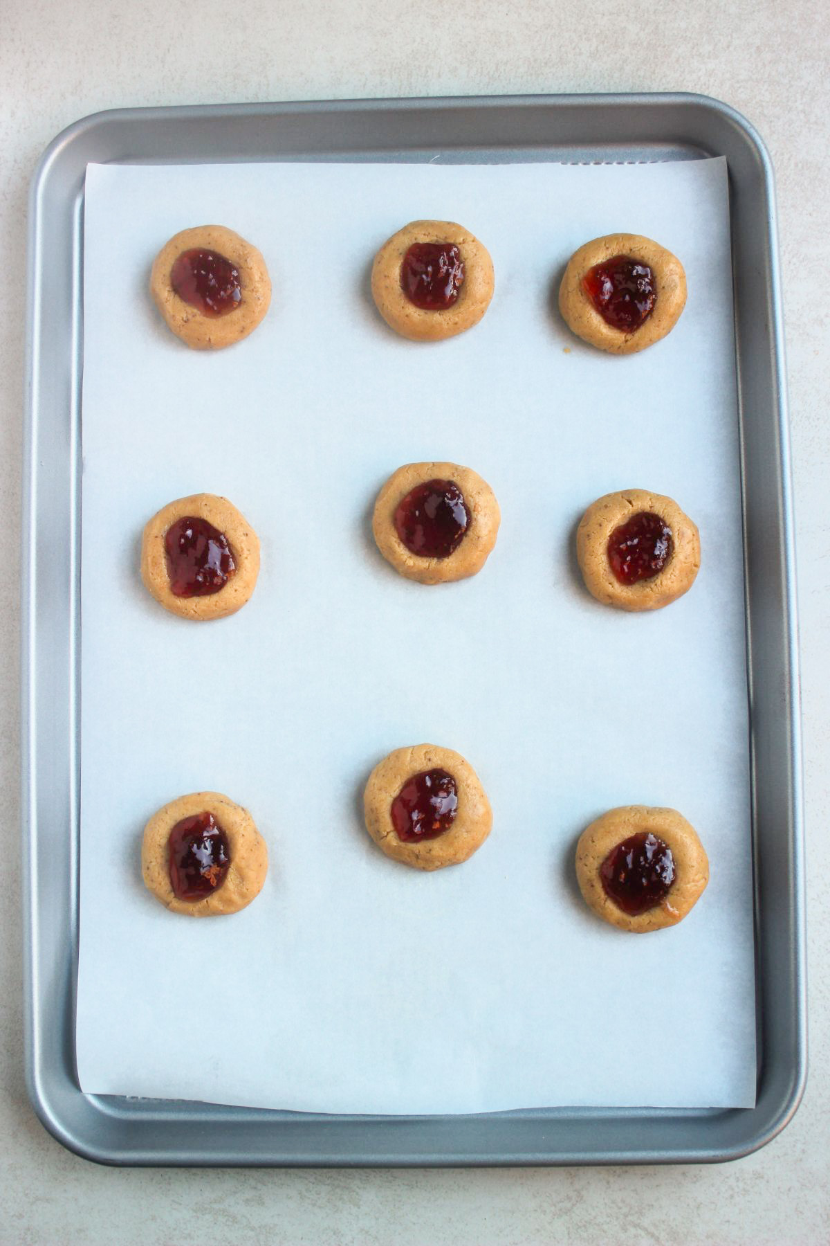 Top view of raw peanut butter thumbprint cookies before baking on parchment paper on a baking sheet.