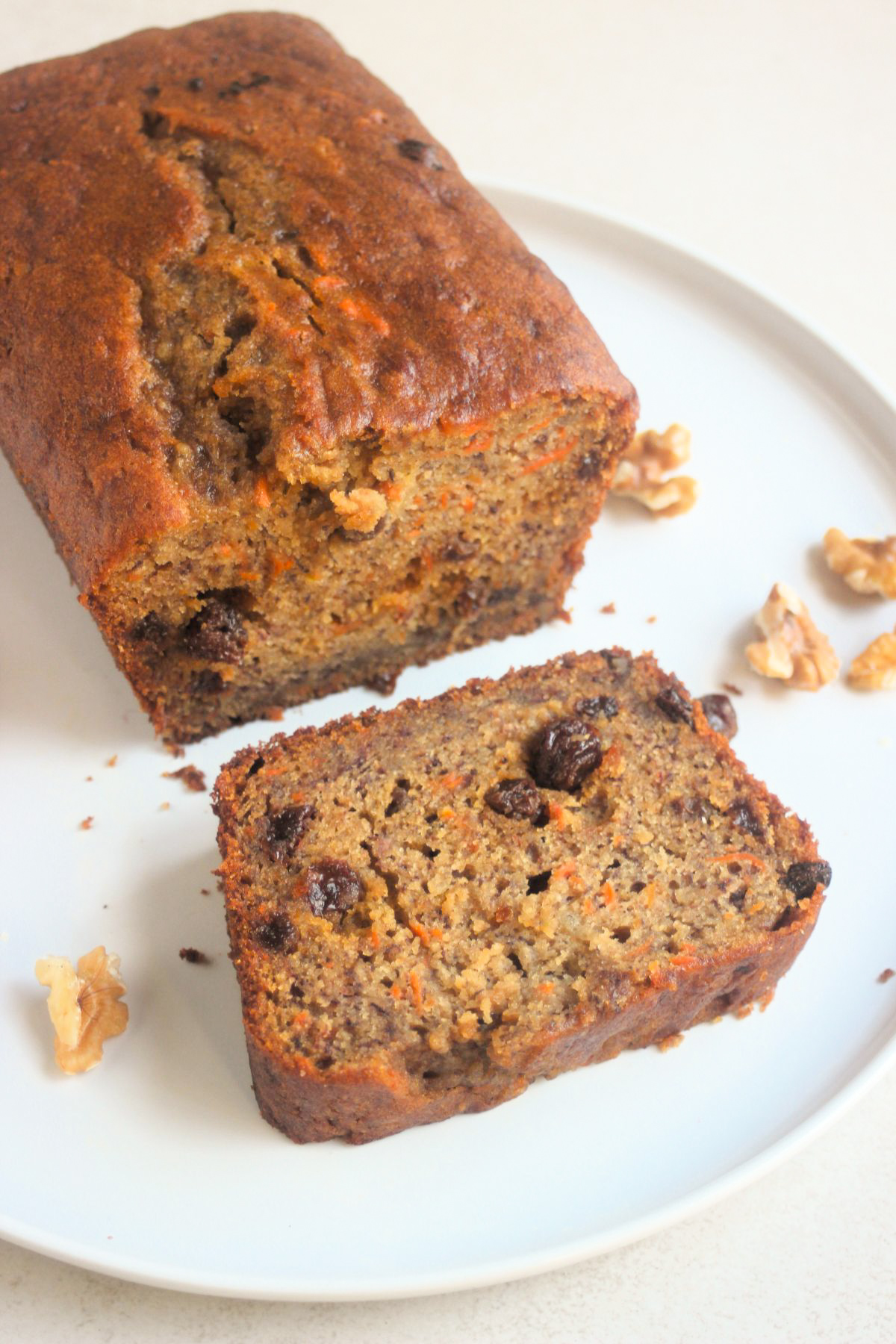 Carrot banana bread with raisinis and a slice of it on a white plate.