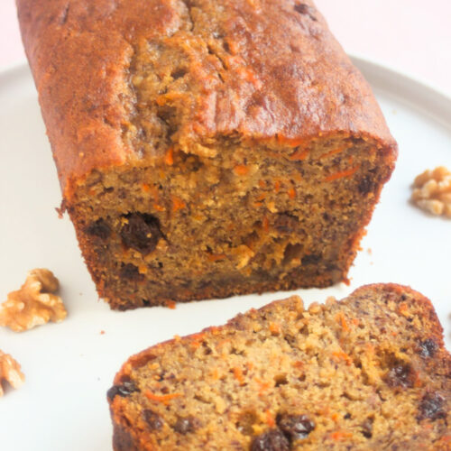 Carrot banana bread with raisinis and a slice of it on a white plate.