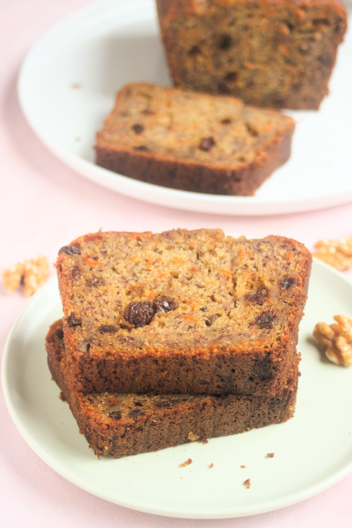 Two slices of carrot banana bread on a plate. Behind, another slice and the whole bread on a white plate.