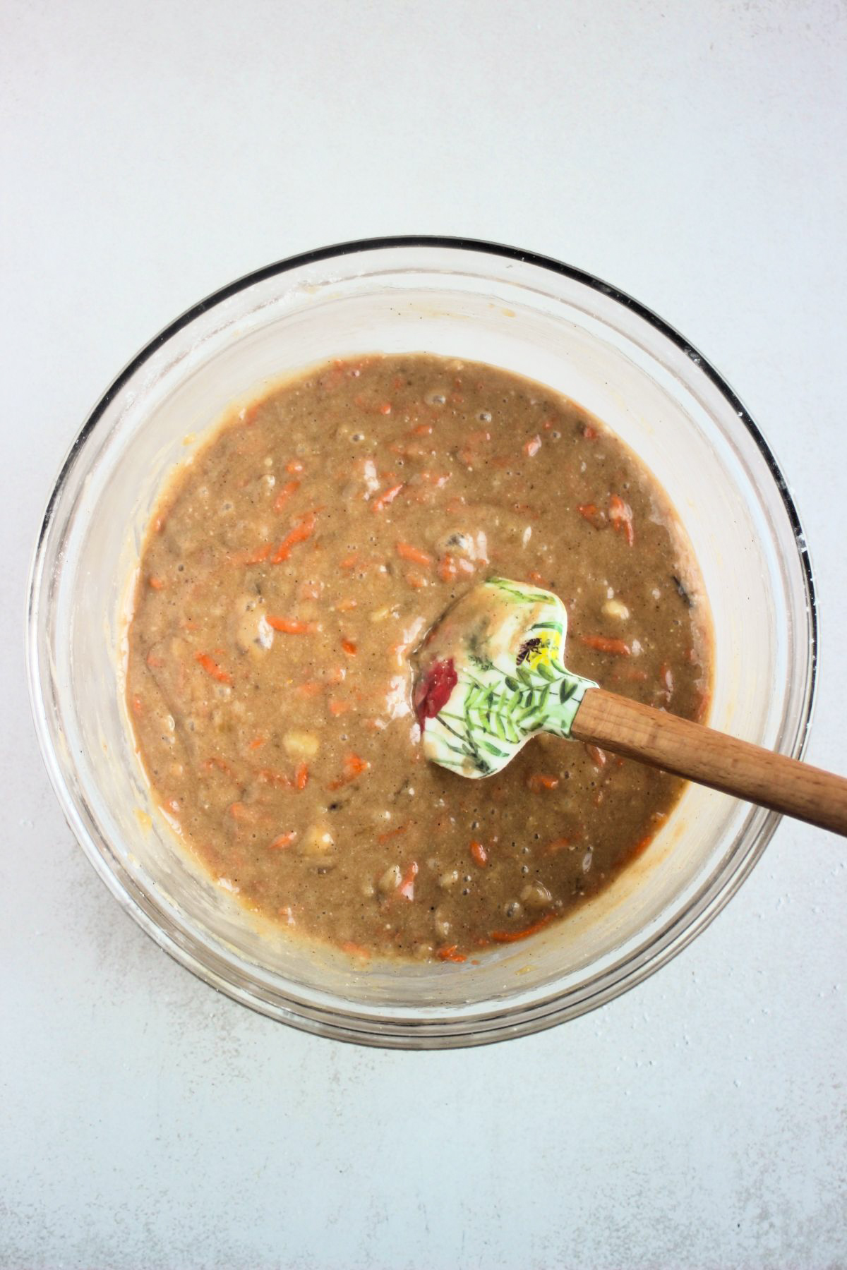 Glass bowl with a brown mixture that includes and a rubber spatula.