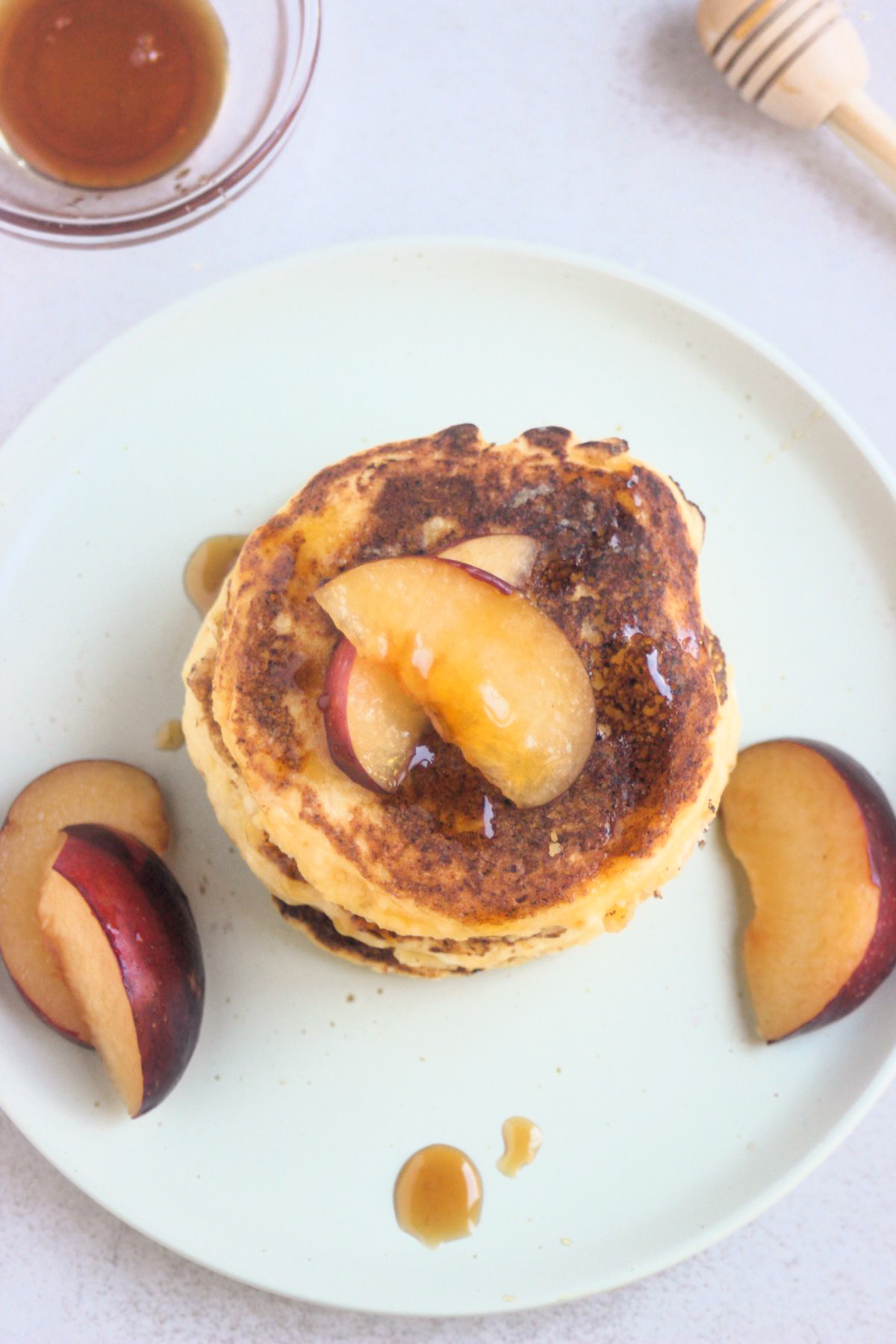 Top view of cottage cheese pancakes stacked on a white plate with fresh plum slices.