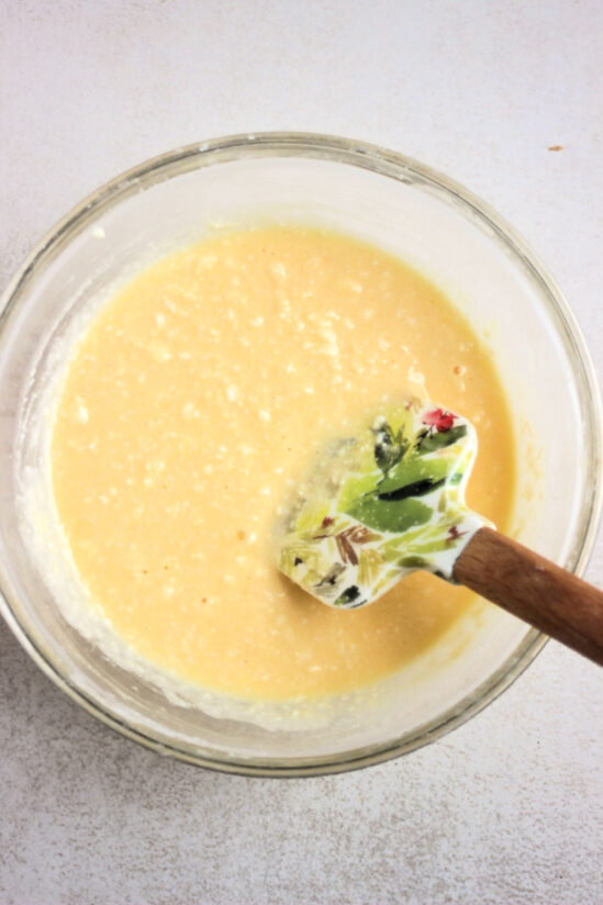 Glass bowl with a cream colour mixture and a rubber spatula.