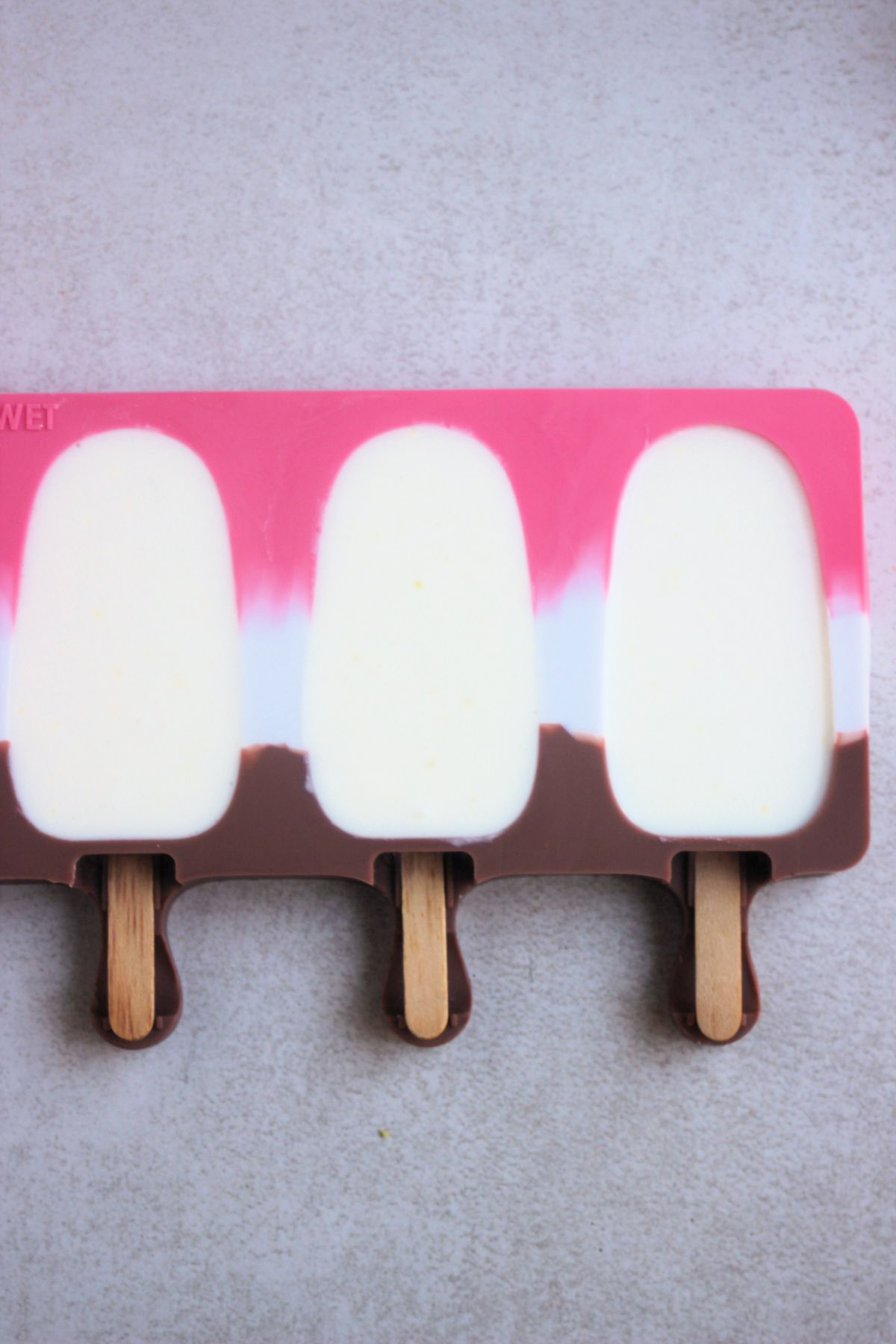 Top view of a popsicle mold fill with a white mixture and sticks added.