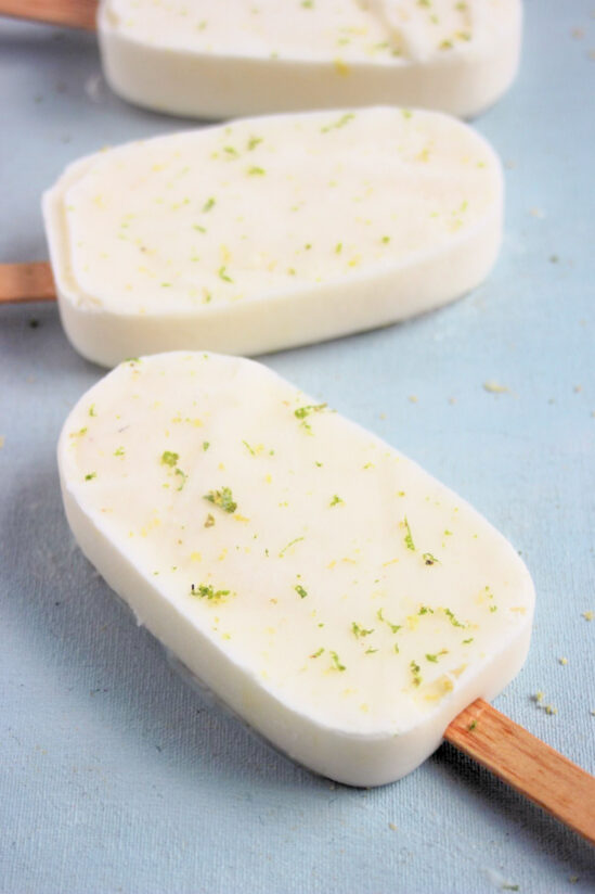 Lime popsicle on a light-blue surface. Other popsicles behind.