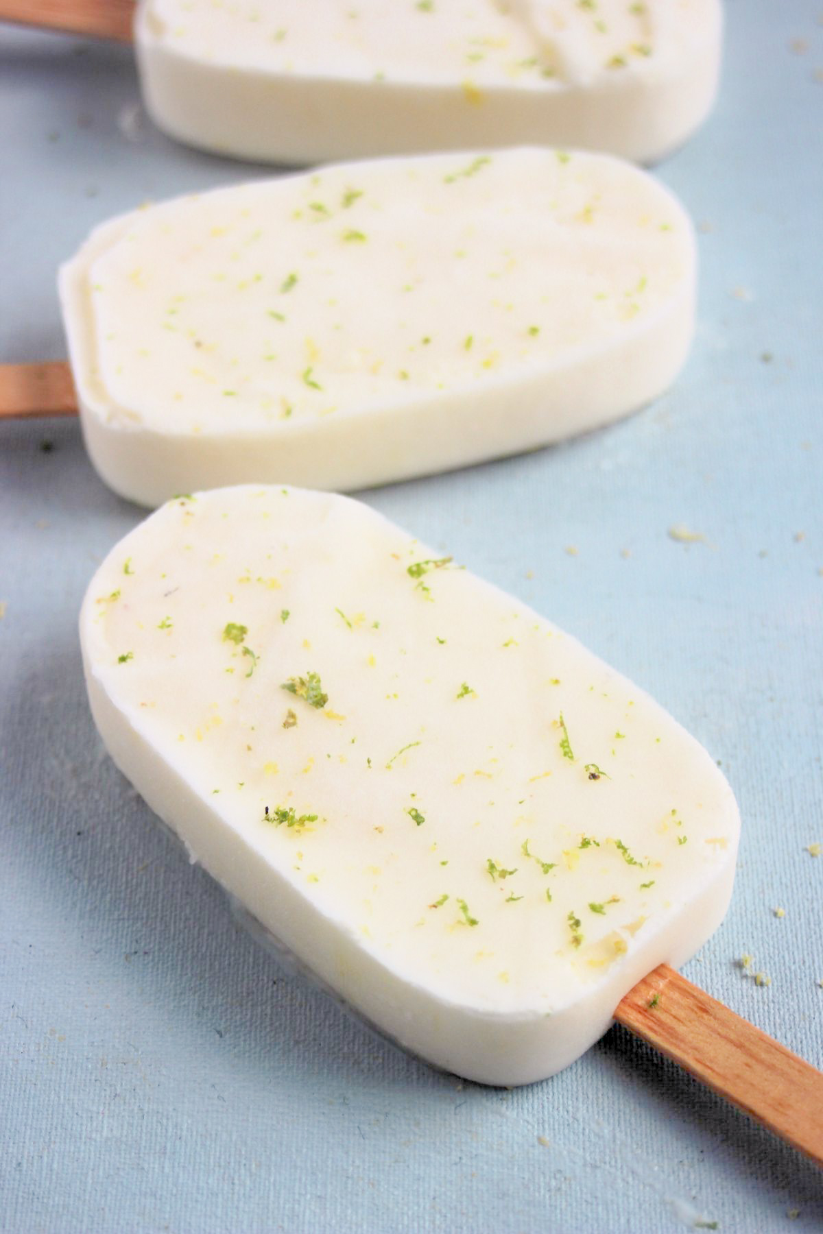Lime popsicle on a light-blue surface. Other popsicles behind.