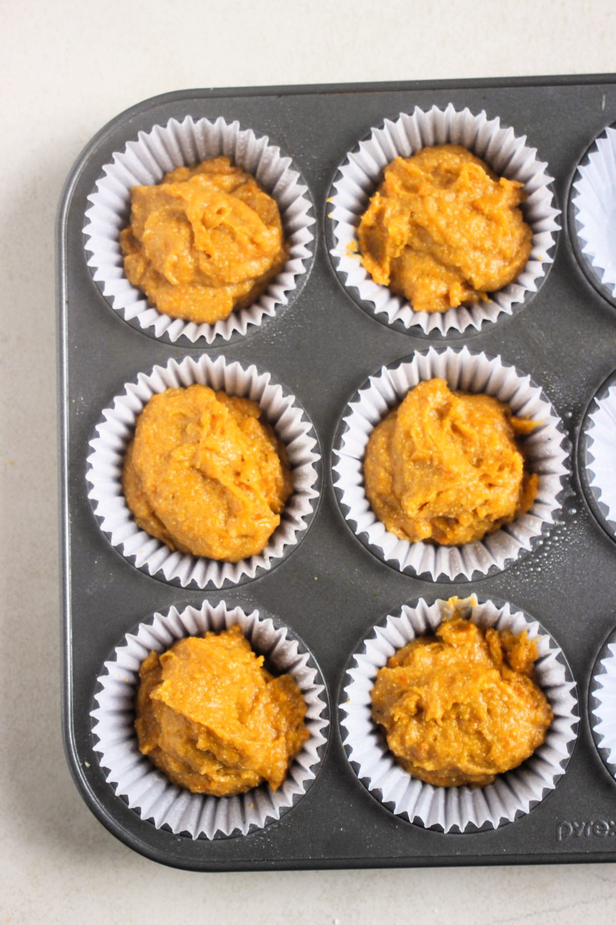 Top view of muffin pan with liners and pumpkin cornbread muffin batter before baking.