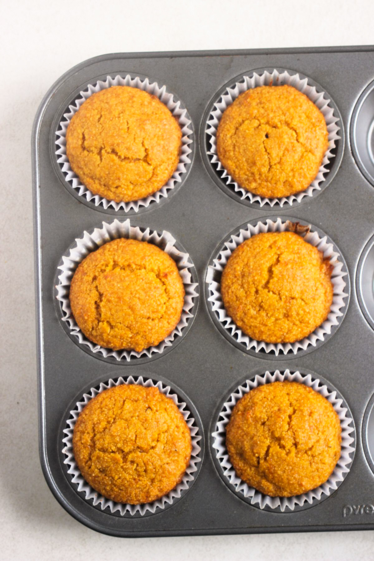 Top view of muffin pan with pumpkin cornbread muffin with liners.