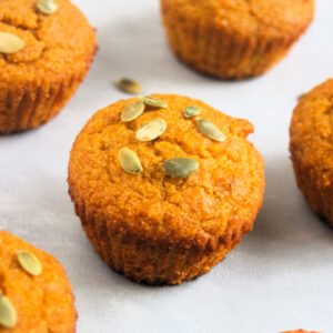Pumpkin cornbread muffins with pumpkin seeds on a white surface.
