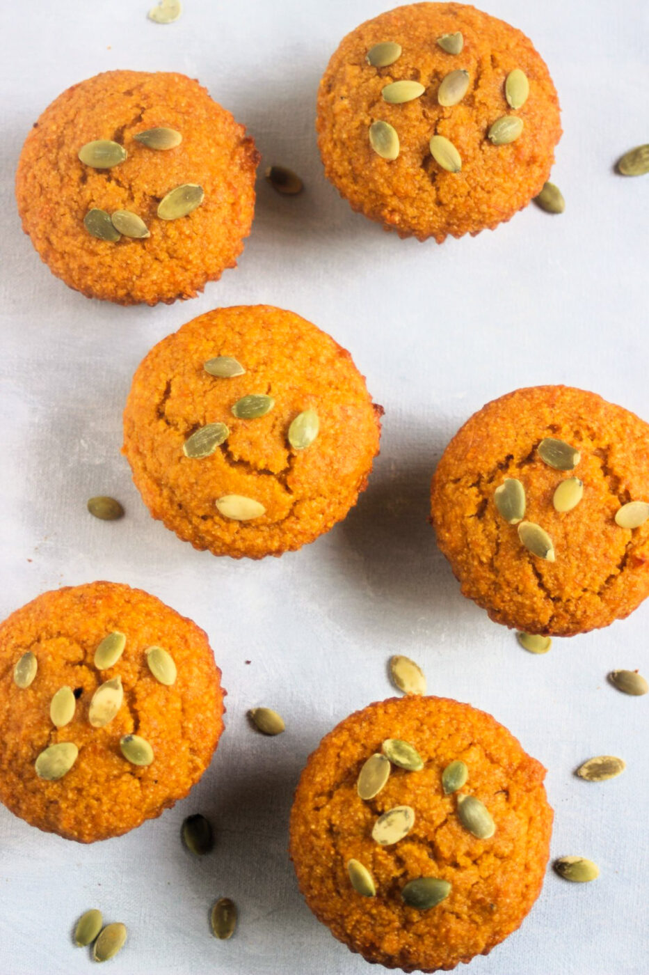 Top view of pumpkin cornbread muffins with pumpkin seeds scattered around on a white surface.