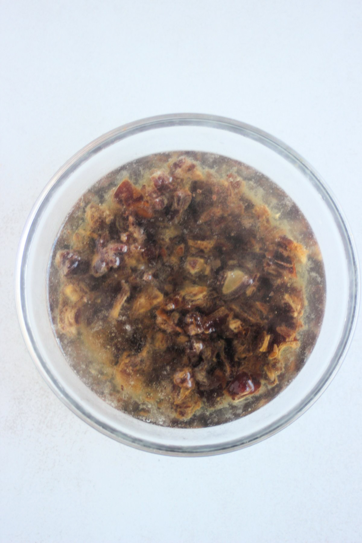 Top view of glass bowl with chopped dates and water.
