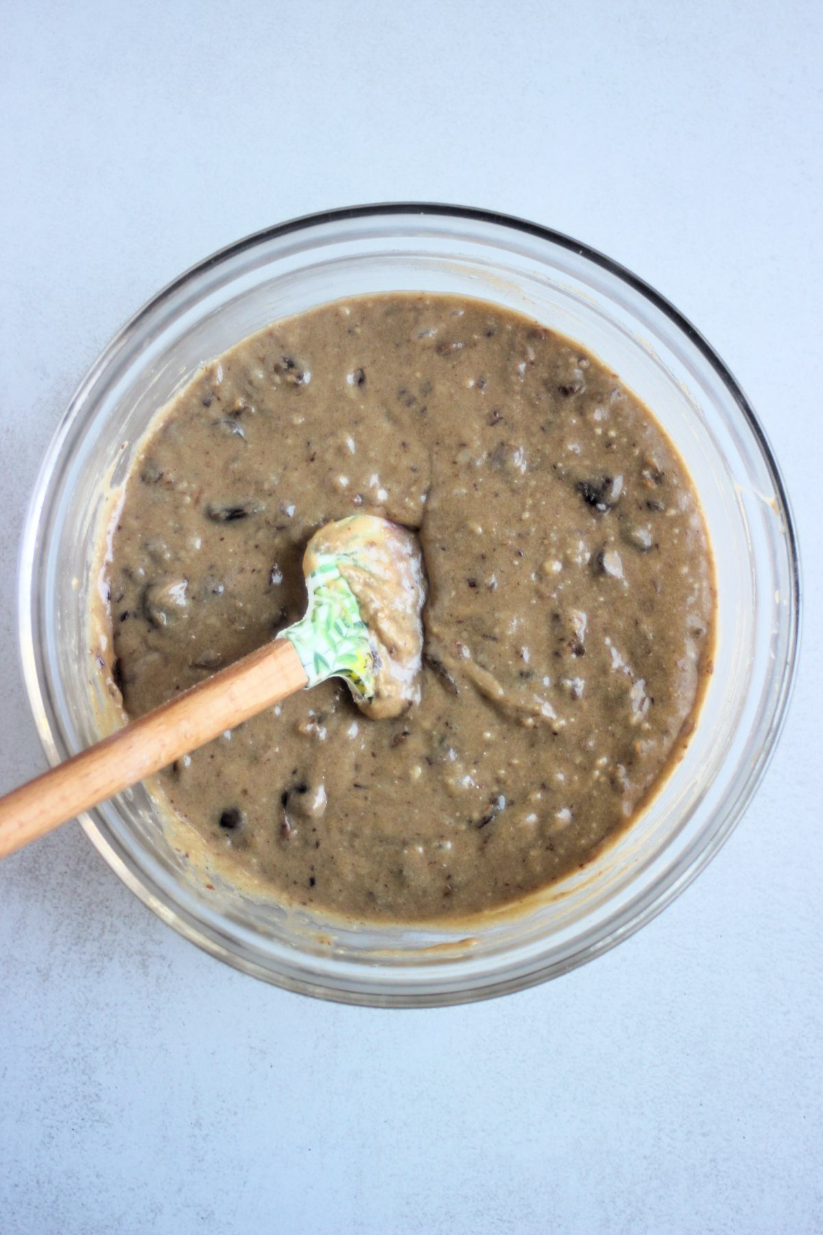 Top view of a glass bowl with a light brown mixture and a rubber spatula.